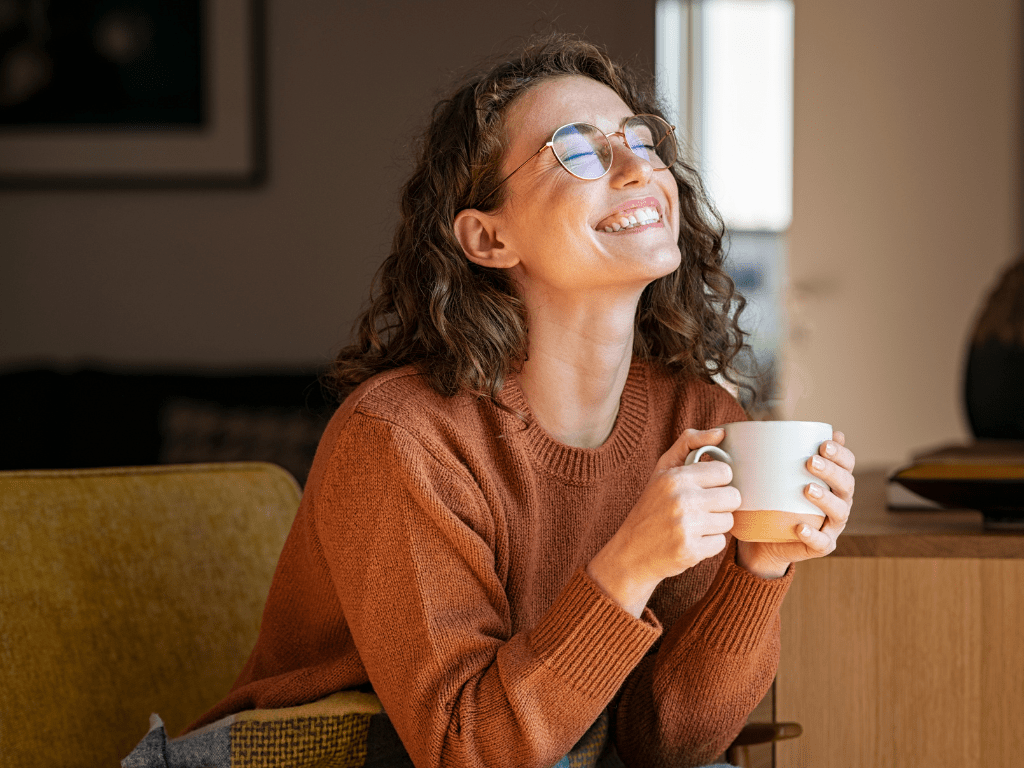 Zu sehen ist eine Frau mit Kaffeetasse. Sie lächelt.