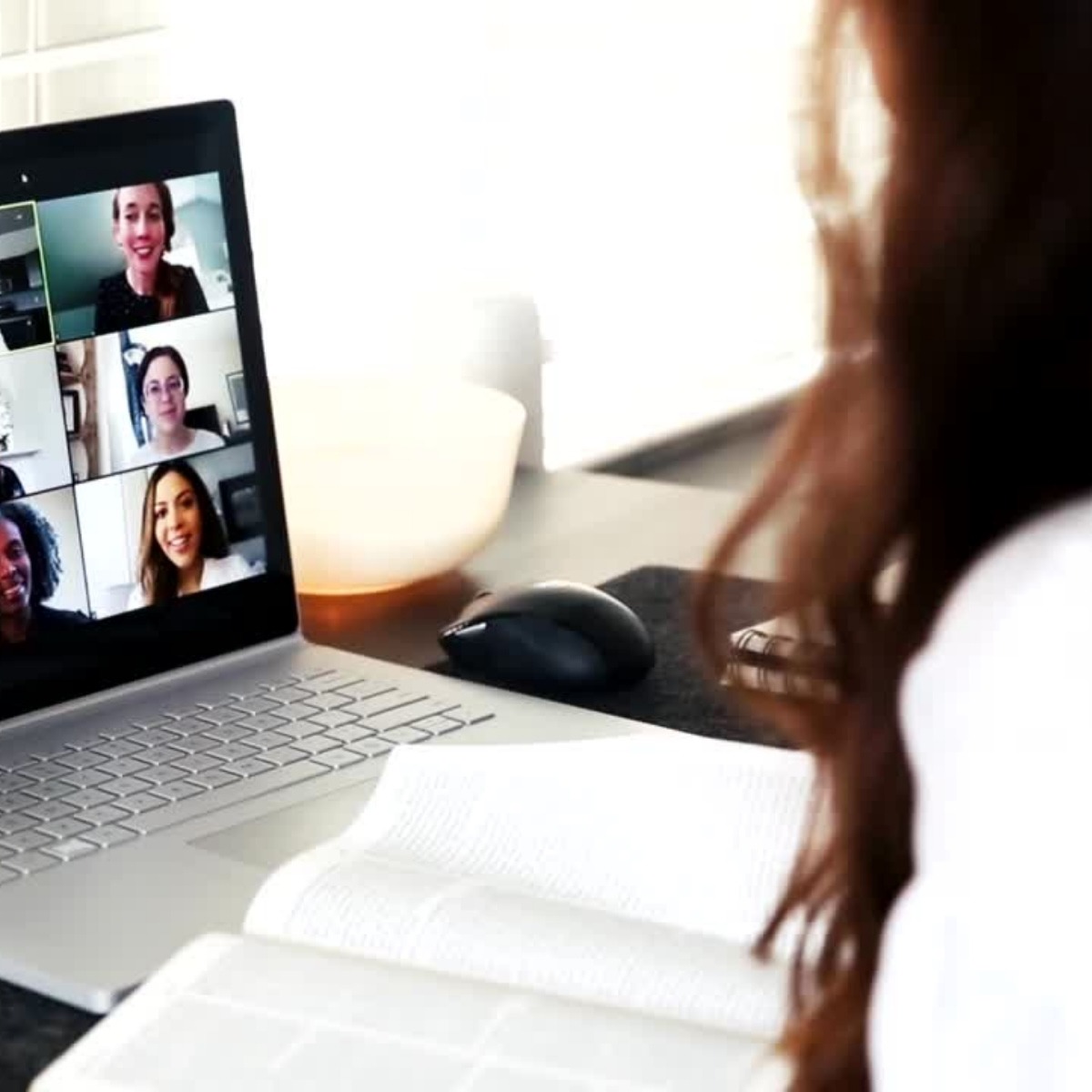 Zu sehen ist eine Frau, die etwas auf ihre Tastatur tippt und eine Videokonferenz ansieht